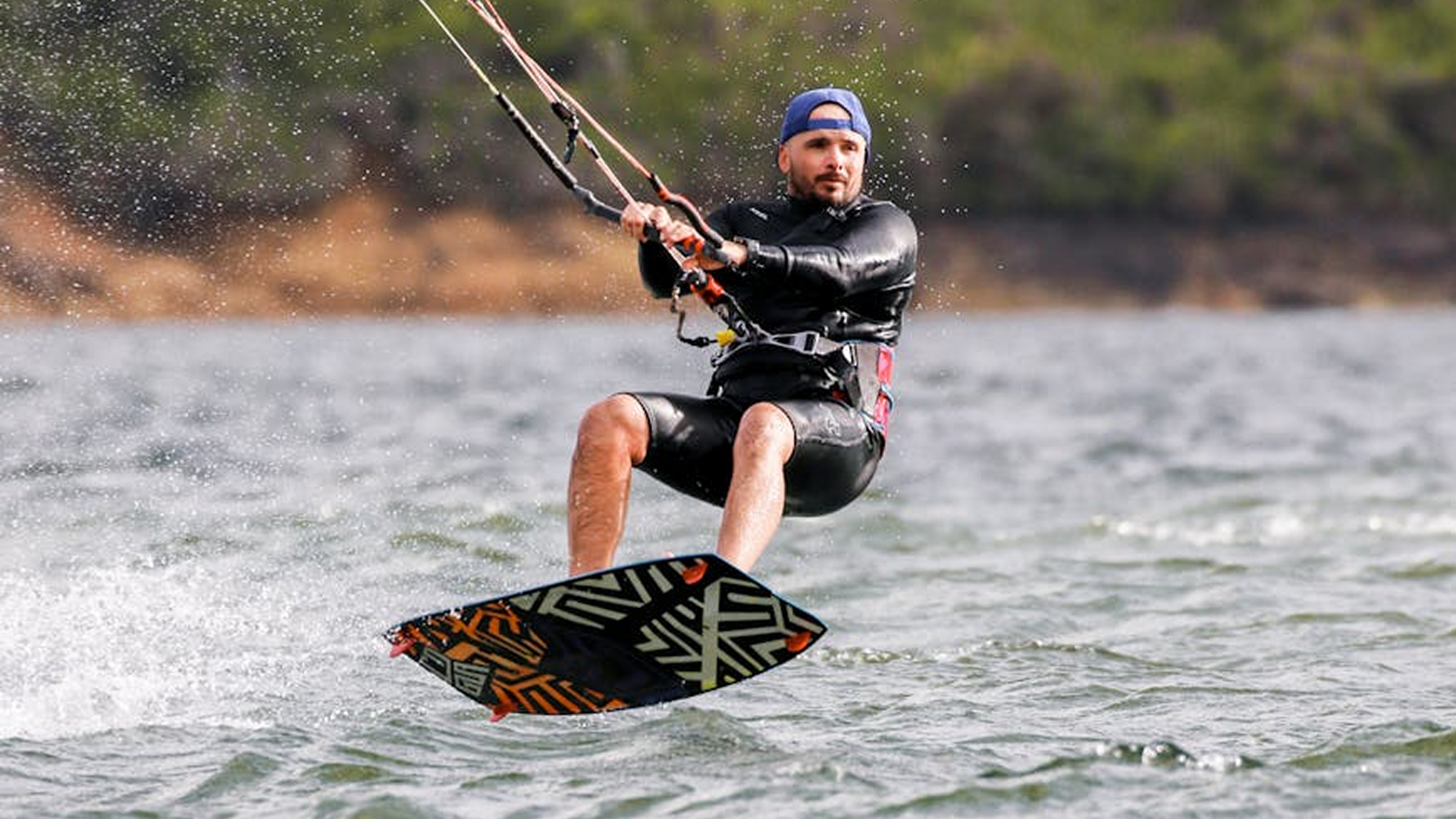 Solo kiteboarder launching a kite on an empty beach, with distant riders in the background under a golden sky