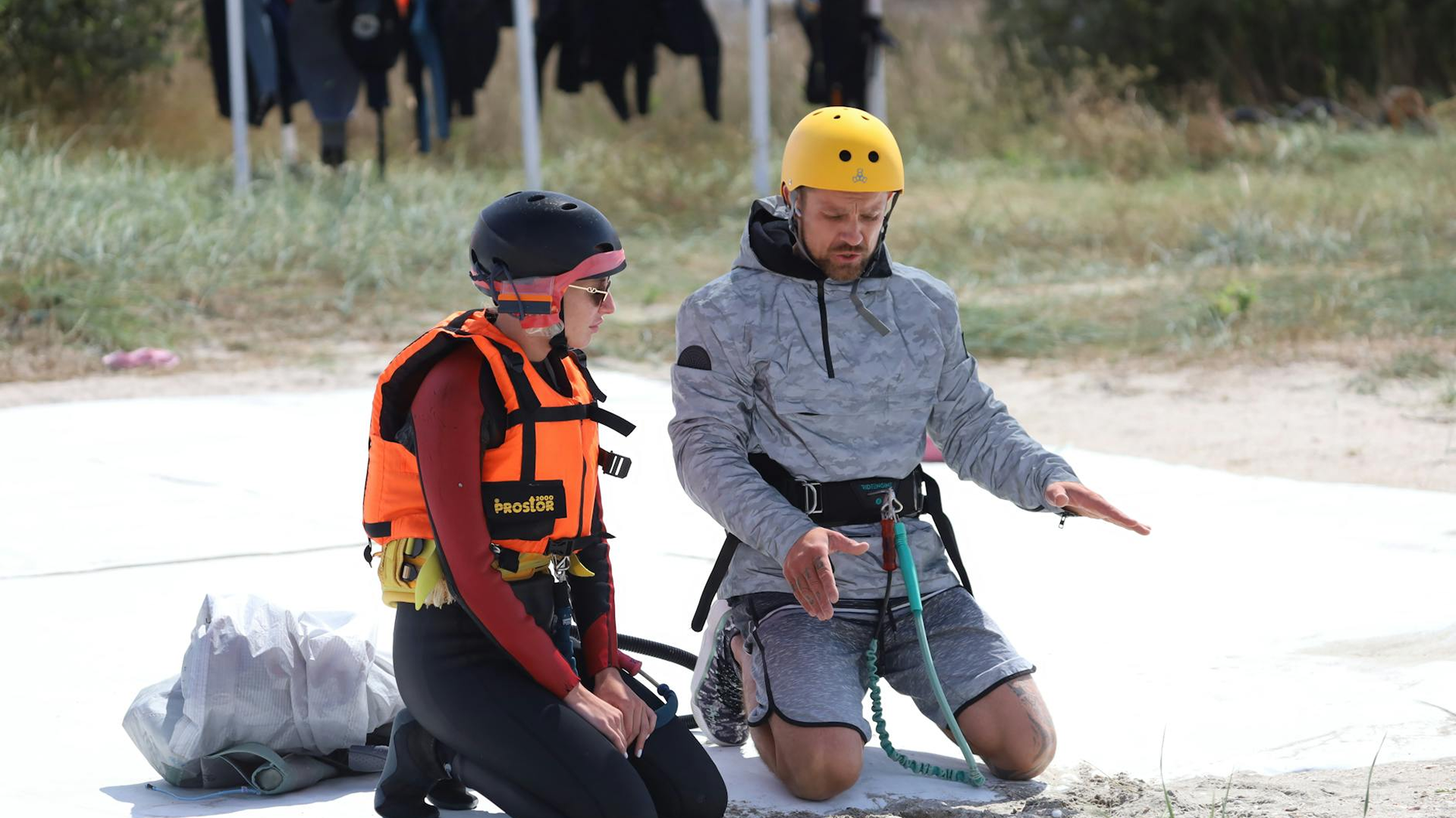 Kiteboarder organizing compact travel gear on a tropical beach with palm trees and kites in the background